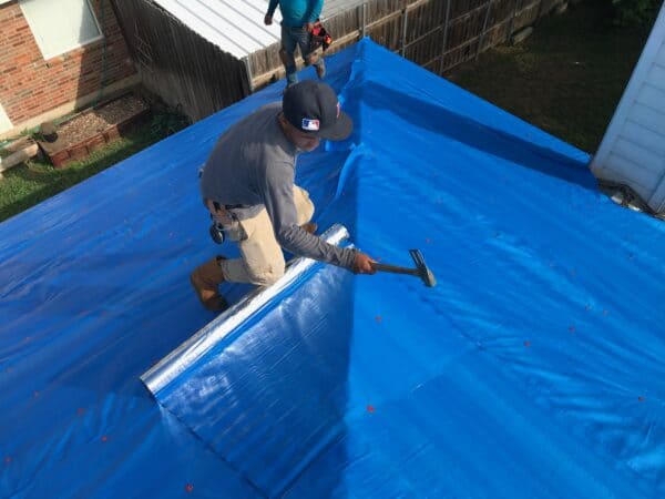 Professional roofer installing ES® RadiantShield Advanced Roof Underlayment on a rooftop with hammer and tacks. This RFID product reflects 95% of radiant heat to help lower energy bills.