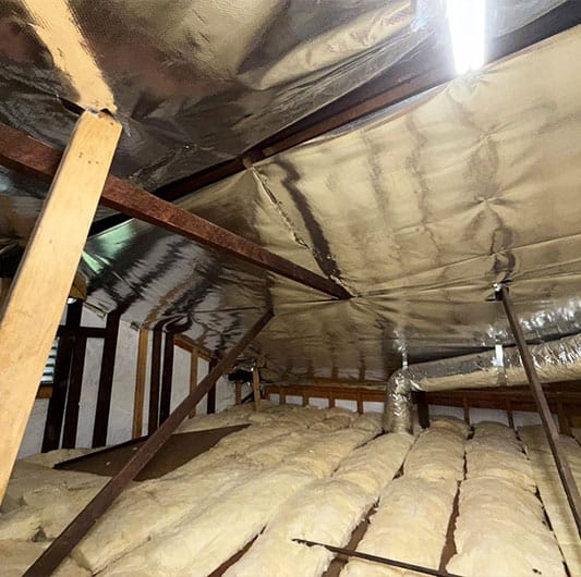 adiant barrier foil under rafters paired with fiberglass batts between ceiling joists in a residential attic.